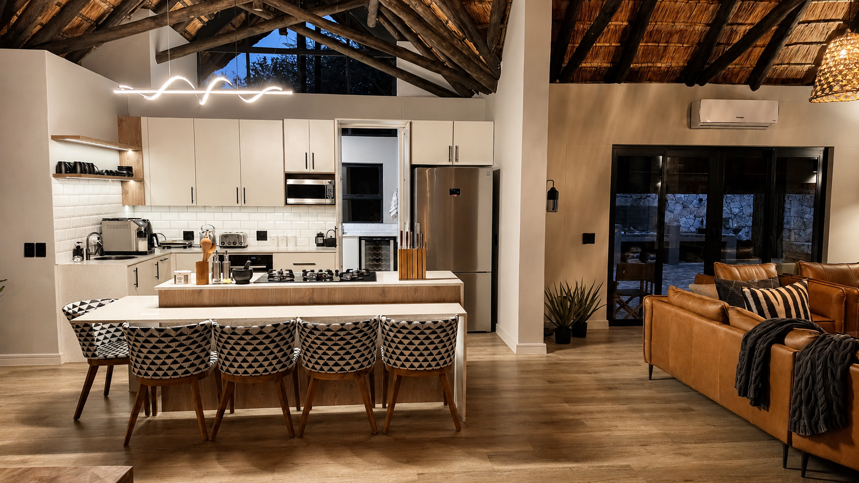 Open-plan kitchen and lounge under the thatched A-frame at dusk.