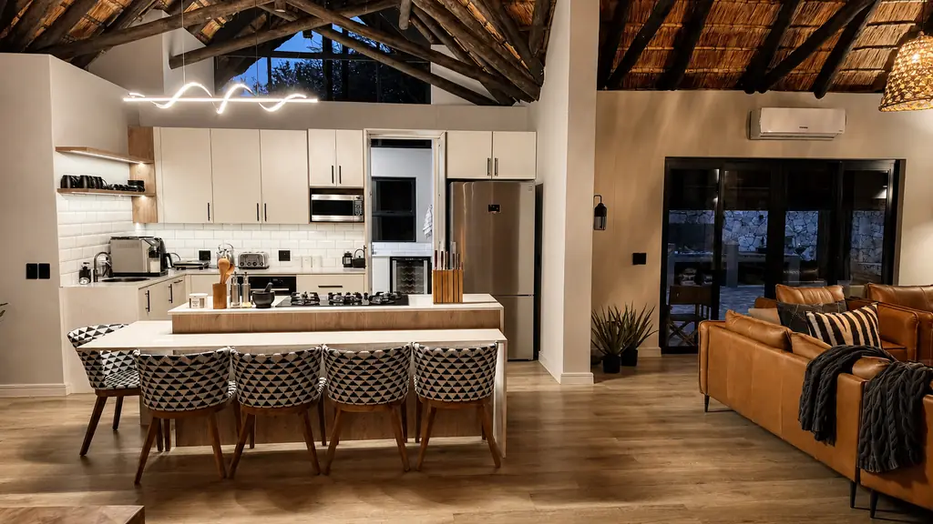 Open-plan kitchen and lounge under thatched A-frame ceiling at dusk
